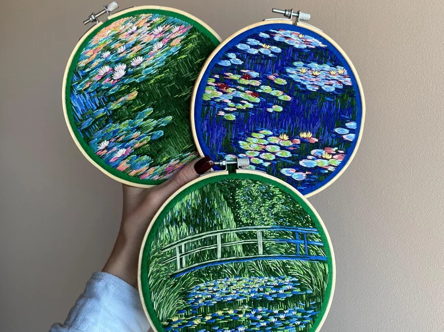 Three embroidered hoops of Monet-style water lilies and a Japanese bridge, held up against a wall