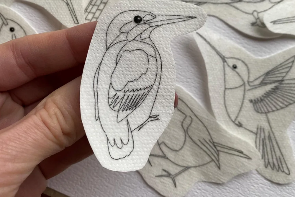 Stick-and-stitch bird embroidery designs, with a kingfisher pattern held up in a hand